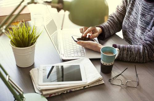 Real Estate agent sitting at a desk with a mobile device, laptop, tablet, and newspaper | Real Estate Promotion